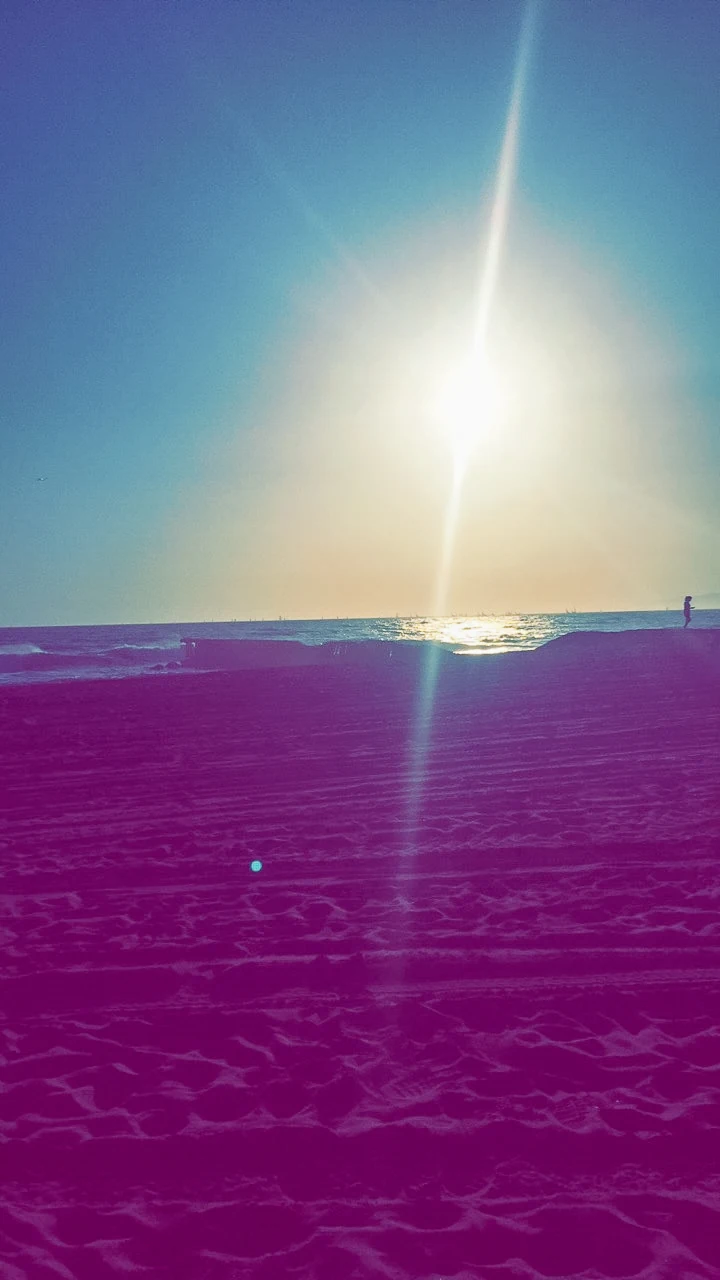 Bright sunlight over a beach with a colorful pink and blue sun flare