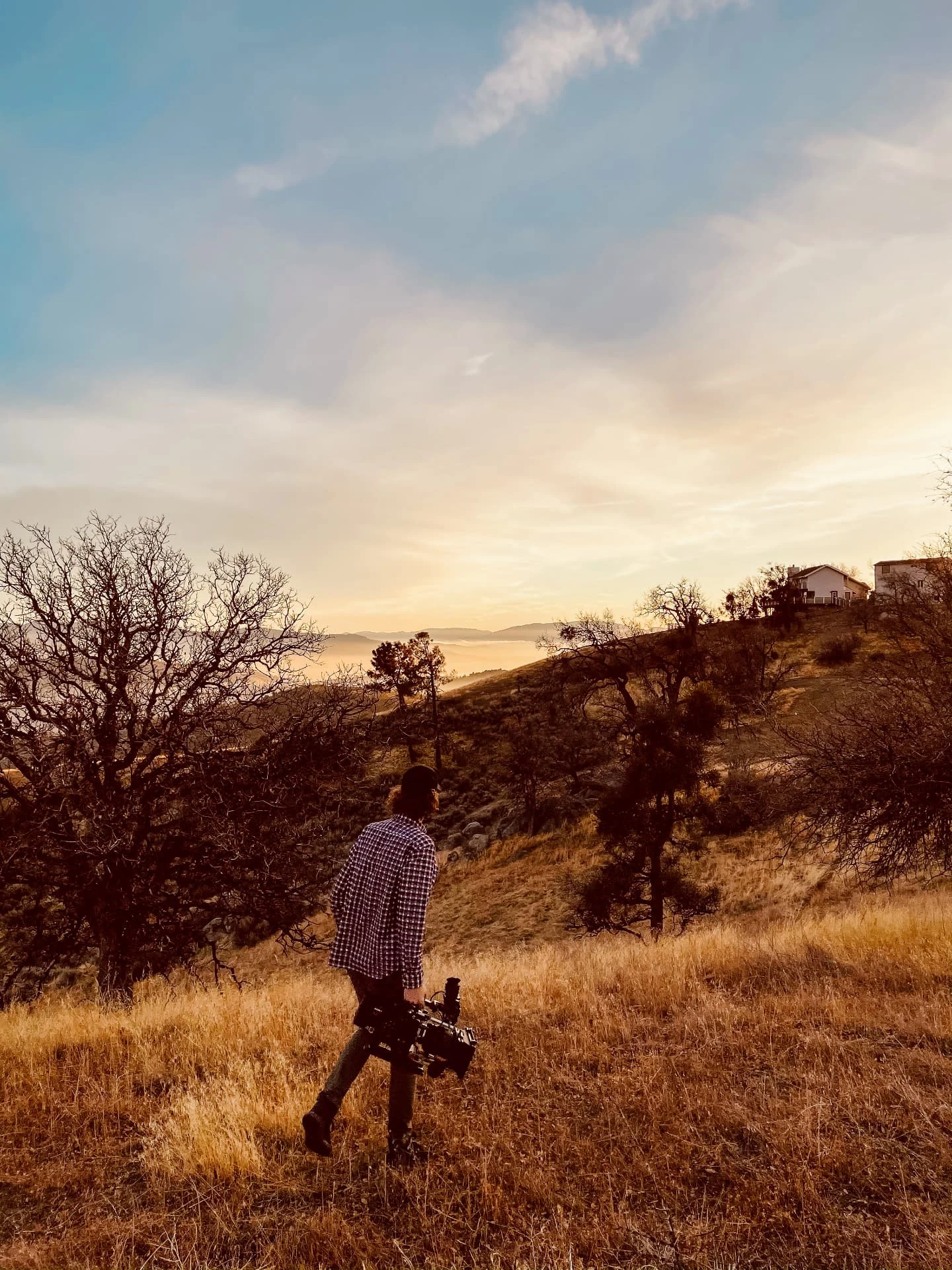 A filmmaker carrying camera equipment through a golden hillside in Tehachapi