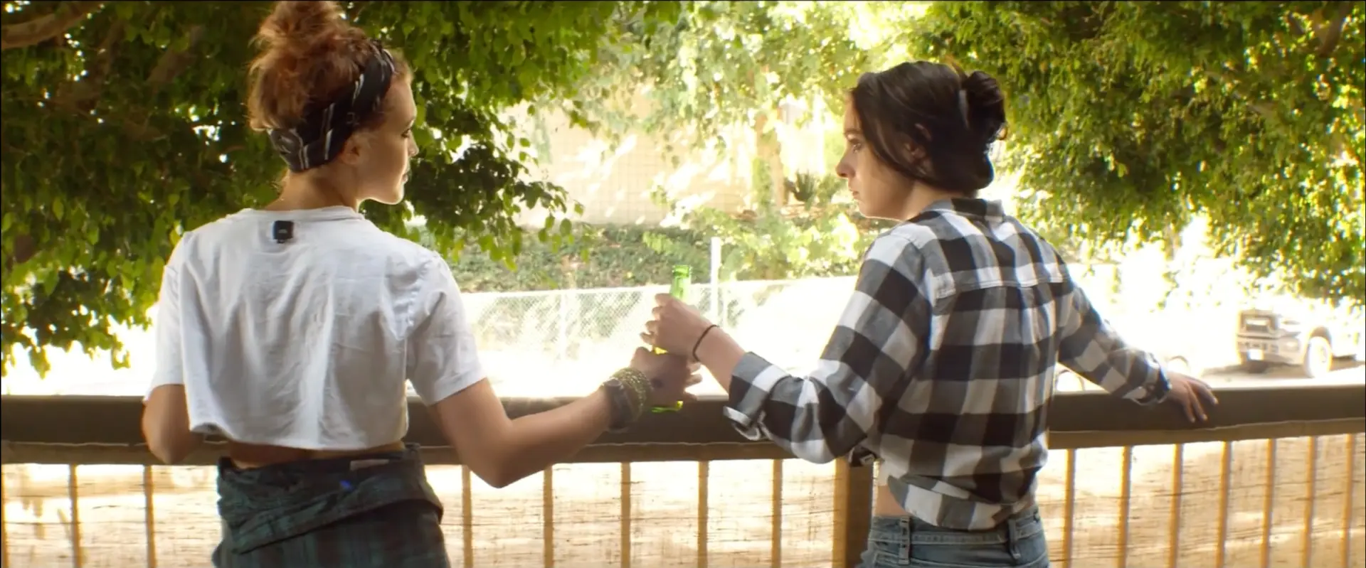 Farewelling film still: two women sharing a drink beneath a leafy tree